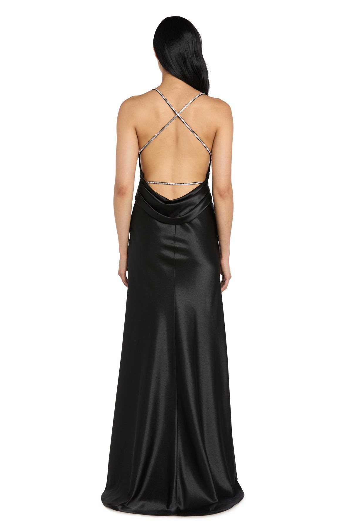 A woman wearing the Long Black Satin Prom Dress: Morgan 14011, featuring a floor-length design, low cowl back, and thin crisscross straps, stands with her back to the camera.
